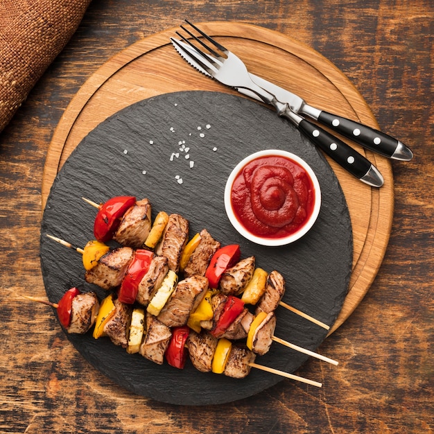 Endecha plana de delicioso kebab en pizarra con salsa de tomate y cubiertos