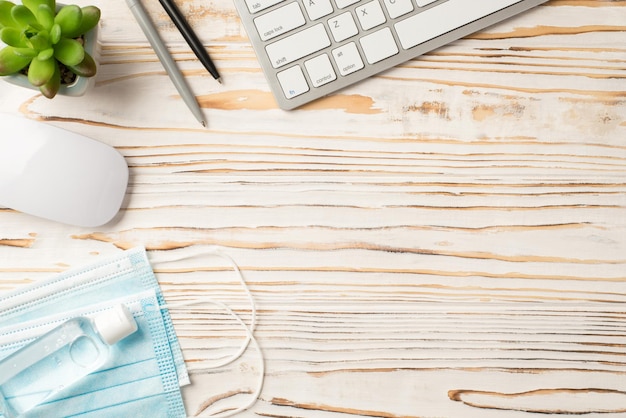 Endecha plana encima de la vista de la foto de la foto de la PC teclado bolígrafos maceta ratón máscaras faciales desechables y antiséptico fondo de madera blanco aislado con espacio en blanco