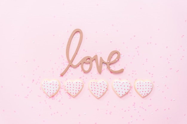 Endecha plana. Galletas de azúcar en forma de corazón decoradas con glaseado real para el Día de San Valentín en un fondo rosa.