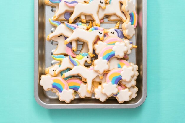 Endecha plana. Galletas de azúcar de unicornio decoradas con glaseado real y purpurina de comida sobre un fondo azul.