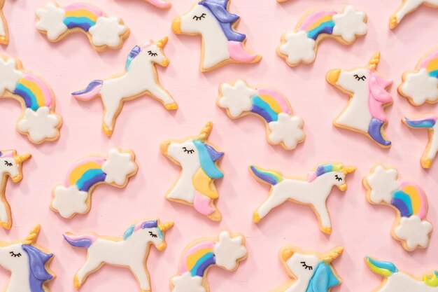 Endecha plana. galletas de azúcar de unicornio decoradas con glaseado real y purpurina de comida sobre un fondo rosa.