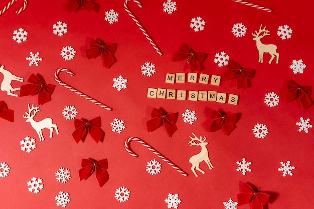 Foto endecha plana con inscripción feliz navidad en un rojo con ciervos, copos de nieve, paletas de rayas.