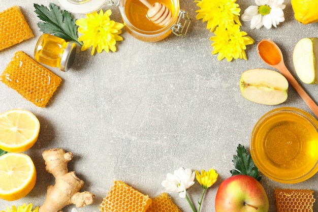 Endecha plana con miel, flores y frutas sobre fondo gris, espacio de copia