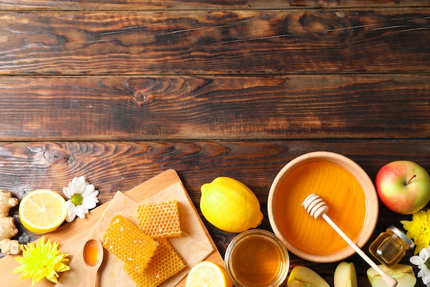 Endecha plana con miel, flores y frutas sobre fondo de madera, espacio para texto