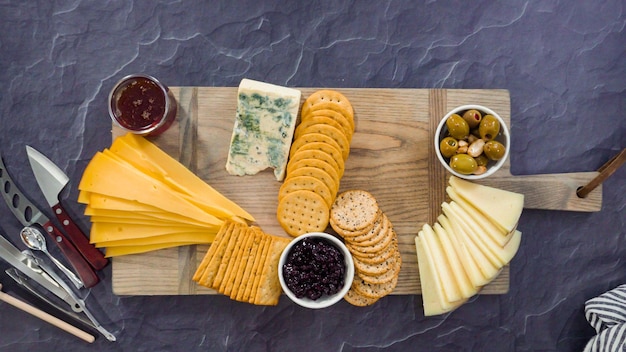 Endecha plana. Organizar queso gourmet, galletas saladas y frutas en una tabla para una tabla de quesos grande.