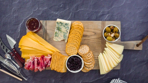 Endecha plana. Organizar queso gourmet, galletas saladas y frutas en una tabla para una tabla de quesos grande.