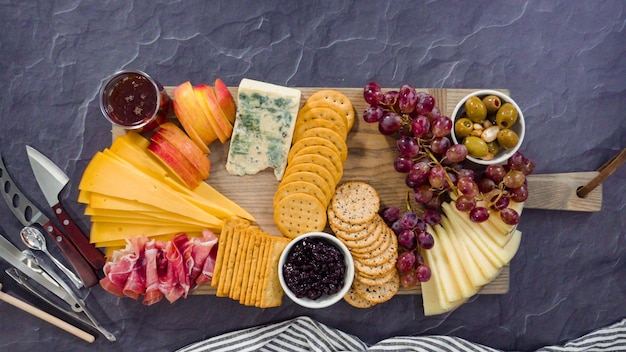 Endecha plana. Organizar queso gourmet, galletas saladas y frutas en una tabla para una tabla de quesos grande.