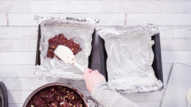 Endecha plana. Paso a paso. Colocar el chocolate derretido en moldes para hornear forrados con papel de aluminio para hacer dulce de nuez de macadamia.