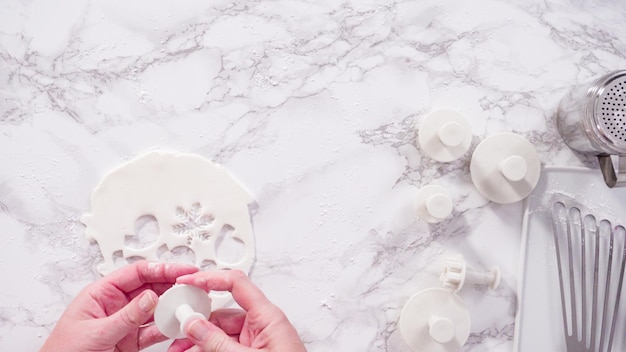 Endecha plana. Paso a paso. Cortar copos de nieve con cortadores de galletas de fondant blanco en un mostrador de mármol.