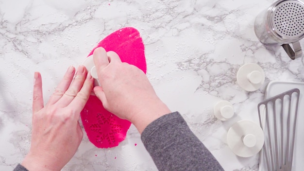 Endecha plana. Paso a paso. Cortar copos de nieve con cortadores de galletas de fondant rosa en un mostrador de mármol.