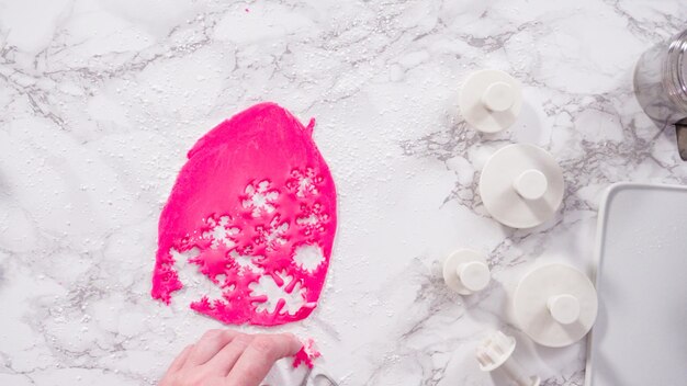 Endecha plana. Paso a paso. Cortar copos de nieve con cortadores de galletas de fondant rosa en un mostrador de mármol.