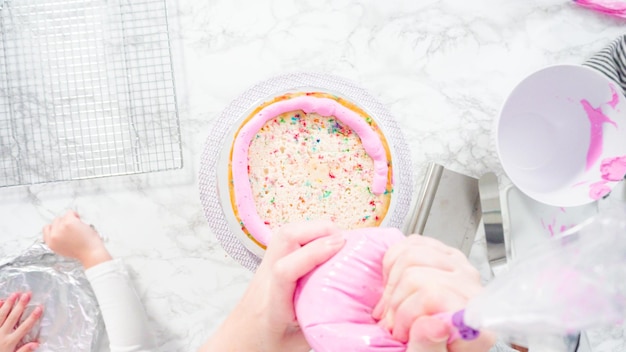 Endecha plana. Paso a paso. Cubre capas redondas de pastel funfetti con glaseado de crema de mantequilla rosa.