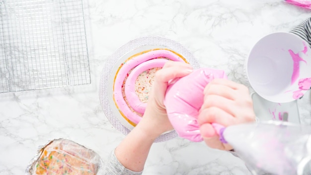 Endecha plana. Paso a paso. Cubre capas redondas de pastel funfetti con glaseado de crema de mantequilla rosa.