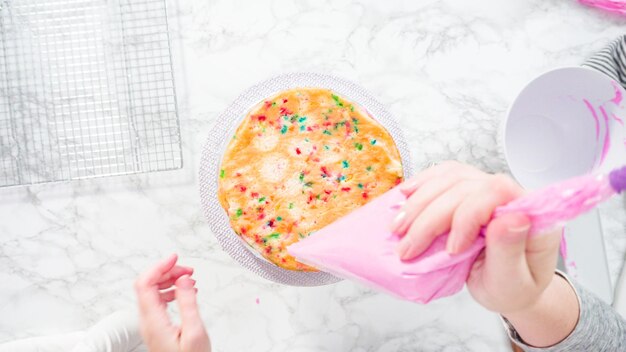 Endecha plana. Paso a paso. Cubre capas redondas de pastel funfetti con glaseado de crema de mantequilla rosa.