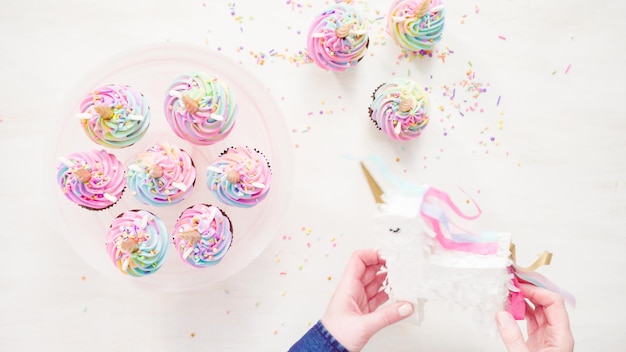 Foto endecha plana. paso a paso. hornear cupcakes de chocolate unicornio con glaseado de crema de mantequilla de color arco iris.