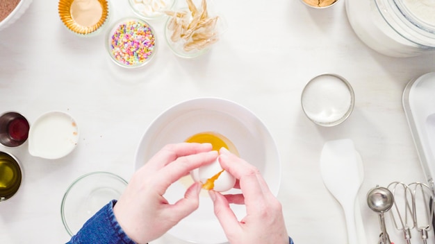 Endecha plana. Paso a paso. Mezcle los ingredientes en un tazón blanco para hacer pastelitos de chocolate de unicornio con glaseado de crema de mantequilla.