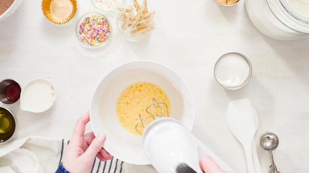 Endecha plana. Paso a paso. Mezcle los ingredientes en un tazón blanco para hacer pastelitos de chocolate de unicornio con glaseado de crema de mantequilla.