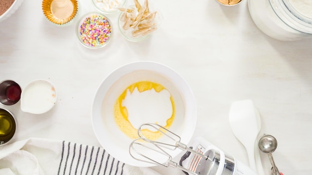 Endecha plana. Paso a paso. Mezcle los ingredientes en un tazón blanco para hacer pastelitos de chocolate de unicornio con glaseado de crema de mantequilla.