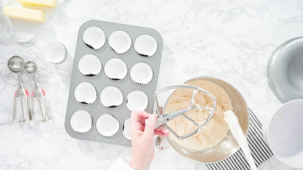 Endecha plana. Paso a paso. Saque la masa con una pala para masa en un molde para cupcakes forrado con moldes de papel para cupcakes.