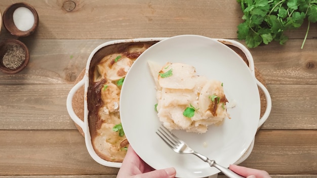 Endecha plana. Patatas gratinadas al horno recién salidas del horno adornadas con perejil en una fuente de horno de cerámica blanca.