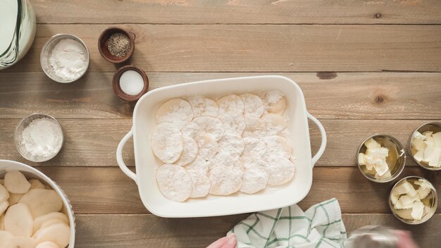 Endecha plana. Preparación de patatas gratinadas en una fuente para horno de cerámica blanca.