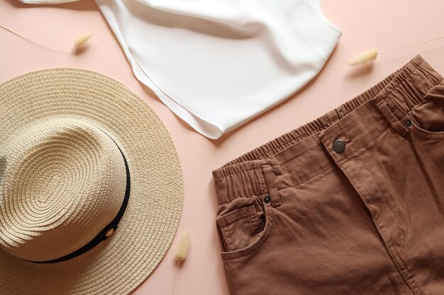 Foto endecha plana de ropa de moda para mujer, pantalones de sombrero de paja y blusa sobre fondo beige