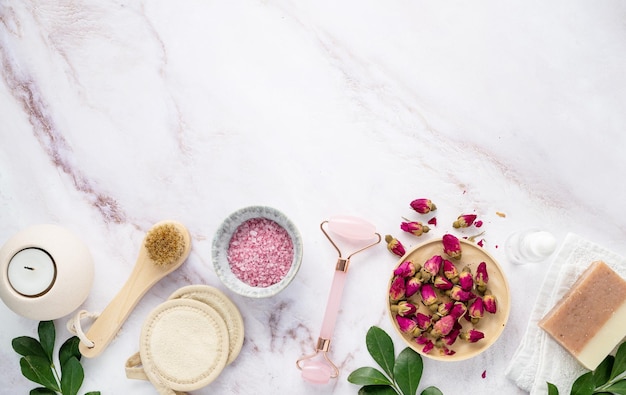 Endecha plana con sal marina orgánica con cepillo de vela de jabón de flores de rosa secas y gua sha sobre un fondo de mármol rosa El concepto de un producto de spa natural Vista superior y espacio de copia