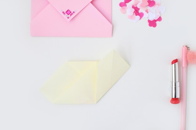 Endecha plana sobre rosa lápiz labial confeti corazones papel amarillo doblado en forma de corazón en la técnica del origami Hacer una postal para el Día de San Valentín Hágalo usted mismo Foto de la serie