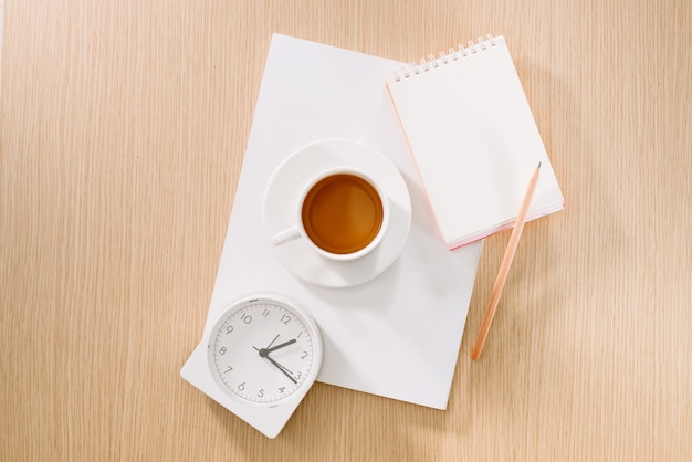 Endecha plana de taza de café, reloj, lápiz y un cuaderno.