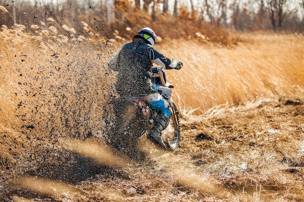 Enduro-fahrer auf einem feld mit trockenem gras im herbst. das motorrad rutscht und macht viele schlammspritzer. fokus auf schlamm