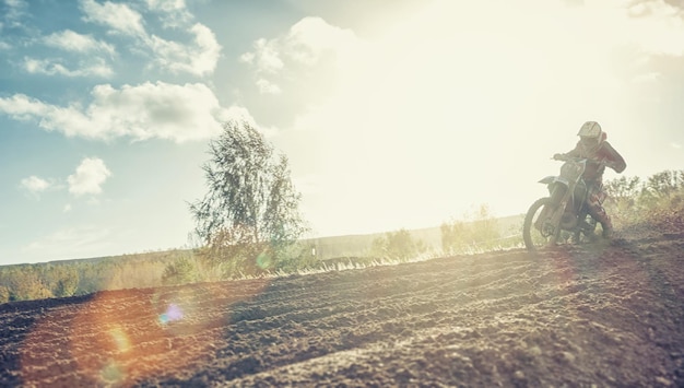 Enduro-Rennfahrer auf Feldweg auf seinem Motocross MX-Zyklus bei Sonnenuntergang