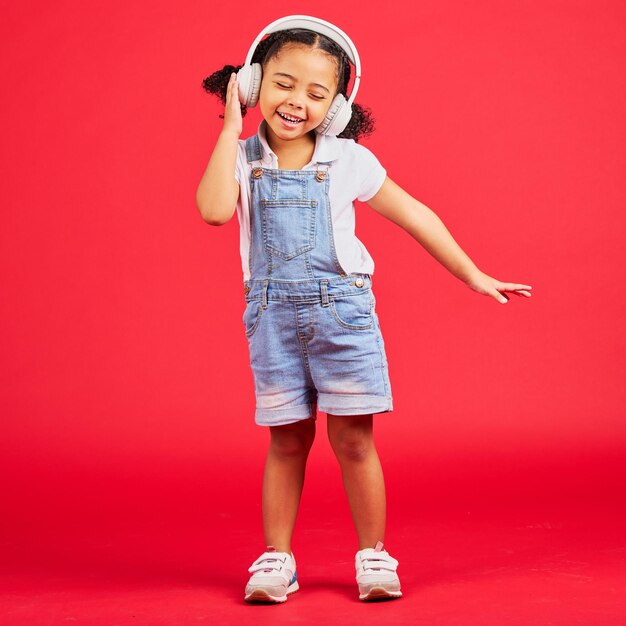 Energía de baile o niña en auriculares de música radio divertida o podcast infantil sobre fondo rojo aislado Sonrisa feliz o niño bailarín escuchando sonido de audio y medios de transmisión en maqueta de estudio