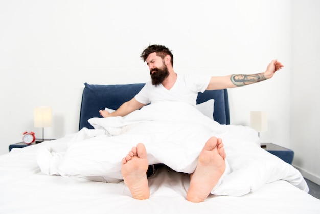 Energía y cansancio de la mañana perezosa Soñoliento y guapo dormido y despierto Demasiado temprano para despertar hombre con barba en pijama en la cama hombre barbudo hipster dormir en la mañana brutal hombre somnoliento en el dormitorio