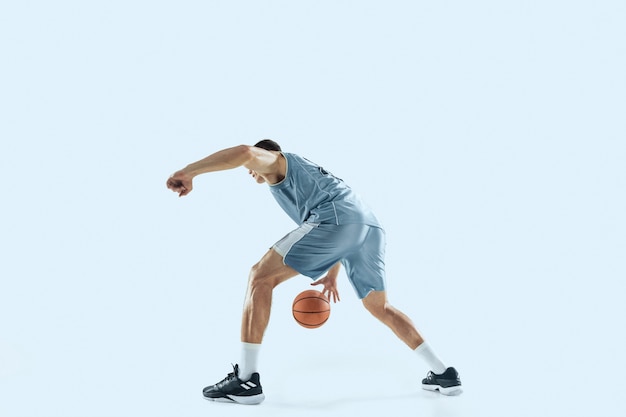 Energia. jovem jogador de basquete caucasiano da equipe em ação, movimento em salto isolado sobre fundo azul. conceito de esporte, movimento, energia e estilo de vida dinâmico e saudável. treinando, praticando.