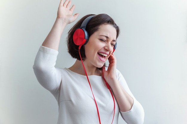 Energía joven dama morena mujer escuchando música en auriculares y cantando aislado en blanco