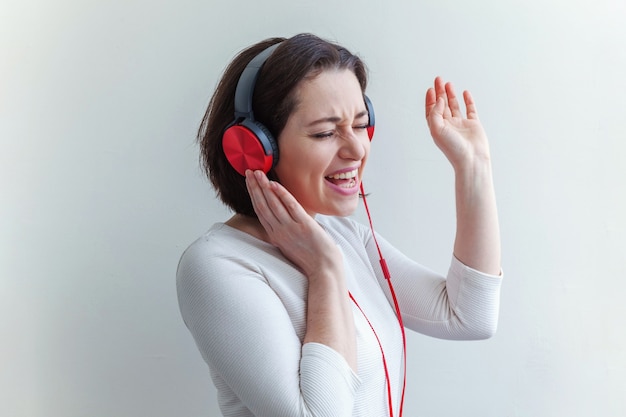 Energía joven dama morena mujer escuchando música en auriculares y cantando aislado sobre fondo blanco.