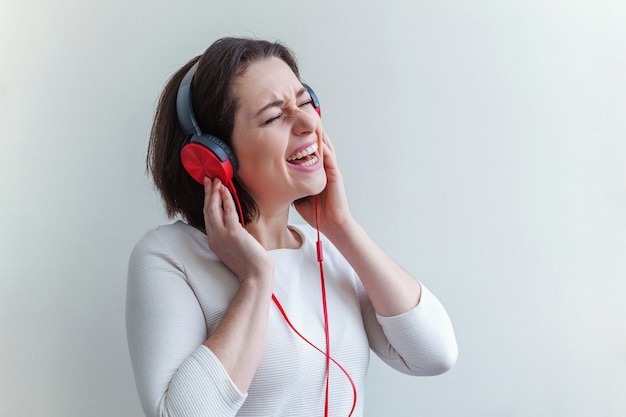 Energía joven morena dama mujer escuchando música en auriculares y cantando aislado en blanco