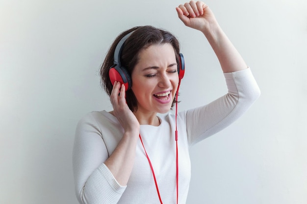 Energie junge brünette Dame Frau hört Musik über Kopfhörer und singt isoliert auf weißem Hintergrund