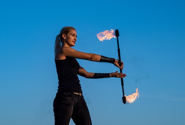 Energie und Eleganz Sexy Mädchen wirbeln flammenden Taktstock blauer Himmel Feuershow Kunstshow oder Performance Baton wirbeln Feiertagsfeier Nachtparty Flamme der Begierde und Leidenschaft