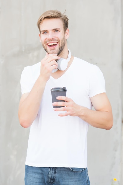 Energie und Optimismus Fröhlicher Kerl hält heiße Tasse im Freien Tee oder Kaffee zum Mitnehmen genießen Onthego Koffein-Energiepause Leckeres Energy-Getränk Morgens Energie tanken Modisches Musik-Accessoire