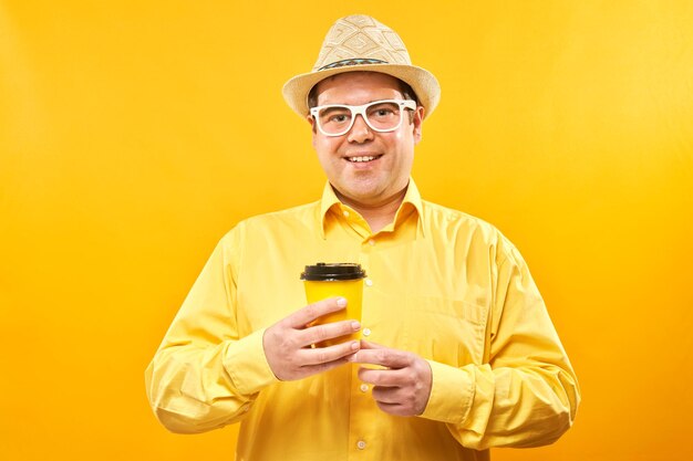 Energiegeladener lustiger Mann, der eine Tasse Kaffee zum Mitnehmen hält und trinkt, lächelt und genießt ein Getränk isoliert auf gelbem Hintergrund