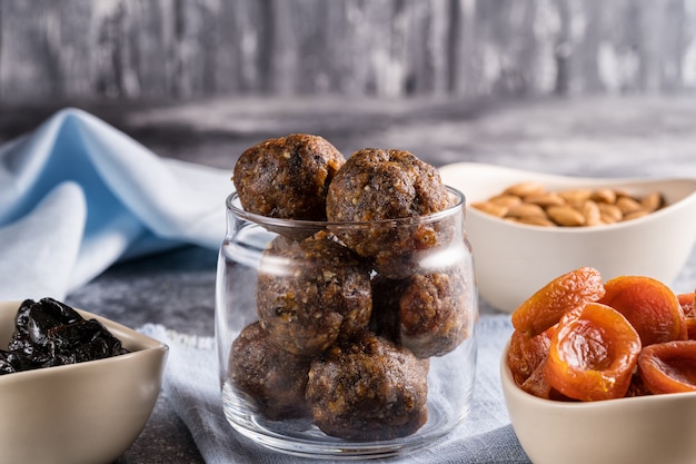 Energiekugeln aus getrockneten Früchten und Nüssen in einem Glas neben den Zutaten für das Kochen von getrockneten Aprikosen, Pflaumen und Mandeln.