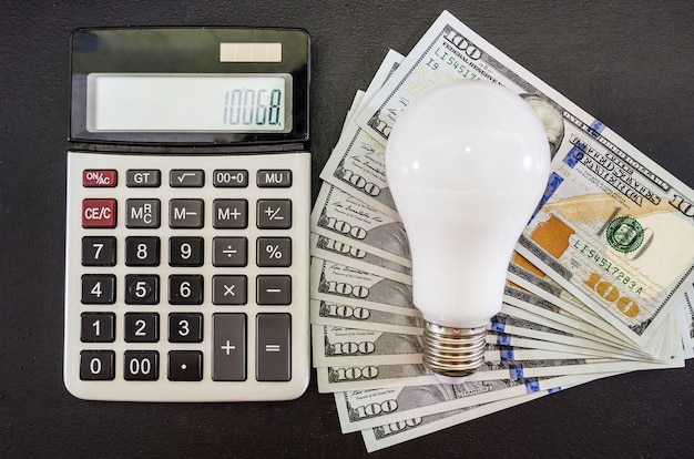 Energiesparkonzept Glühbirne mit Taschenrechner und Dollar auf Schwarz