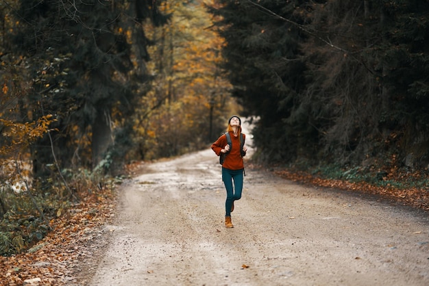 Foto energische frau läuft mit rucksack im herbstwald entlang der straße. hochwertiges foto