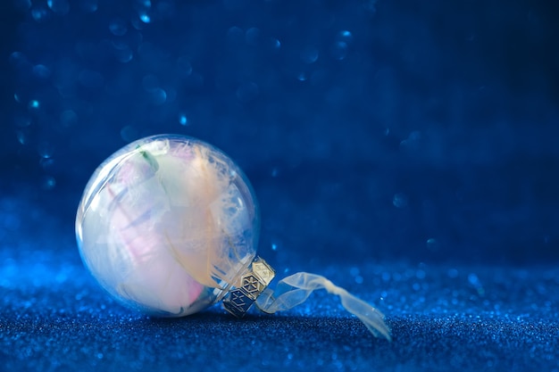 Foto enfeite de bola de vidro preenchido com penas, pequeno presente. enfeite de bola clara com decorações de natal em fundo azul cintilante.