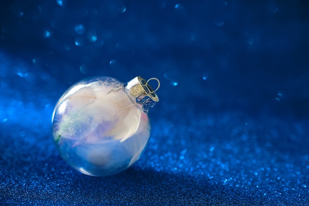 Foto enfeite de bola de vidro preenchido com penas, pequeno presente. enfeite de bola clara com decorações de natal em fundo azul cintilante.