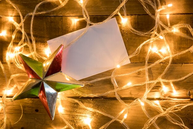 Enfeite de estrela de Natal com papel em branco e luzes de Natal em fundo de madeira vintage