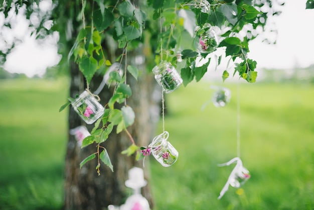 Enfeite frascos com flores penduradas em árvores com folhagem verde