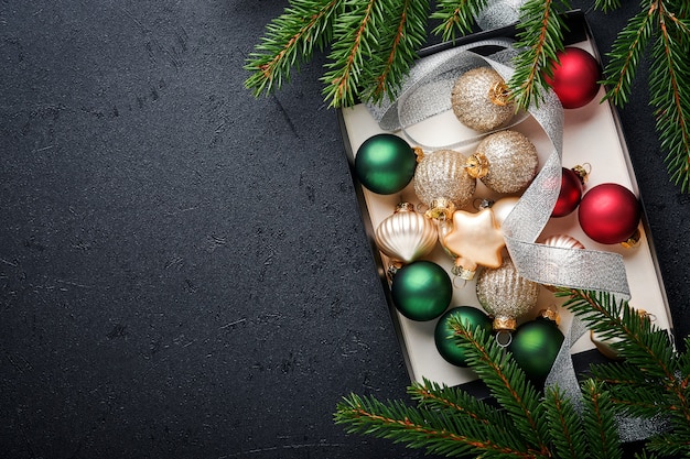 Enfeites de bolas de ouro, vermelho, verde e prata de natal em caixa em fundo preto escuro. decoração de natal. decorações do feriado com enfeites de ouro. projeto de borda. vista superior. cartão de natal.