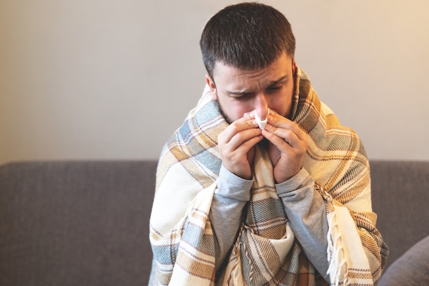 Enfermedad. Anímate en casa. Un joven está enfermo, recibe tratamiento en casa. Se sopla la nariz en una servilleta, secreción nasal. Infección, epidemia, portador de bacilo